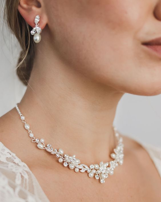 a woman wearing a necklace and earrings with pearls on the neck, in white lace