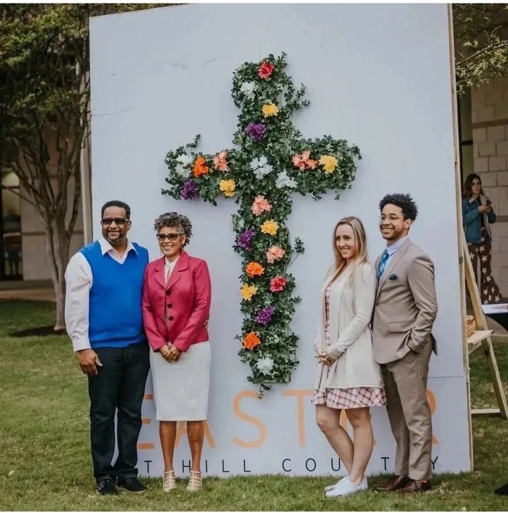 three people standing in front of a cross with flowers on it