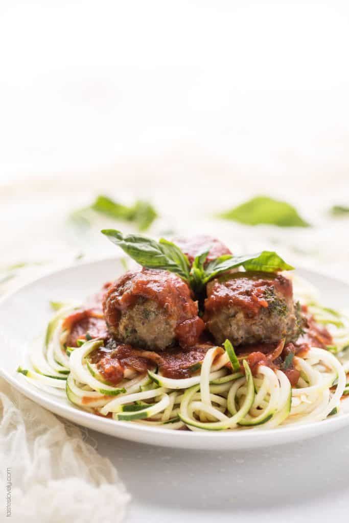 spaghetti with meatballs and tomato sauce on it in a white plate next to a green leafy garnish