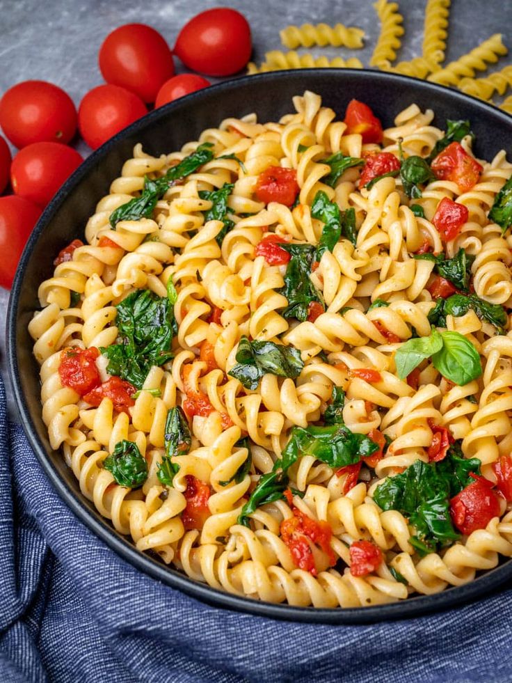 pasta with spinach and tomatoes in a skillet on a blue towel next to cherry tomatoes