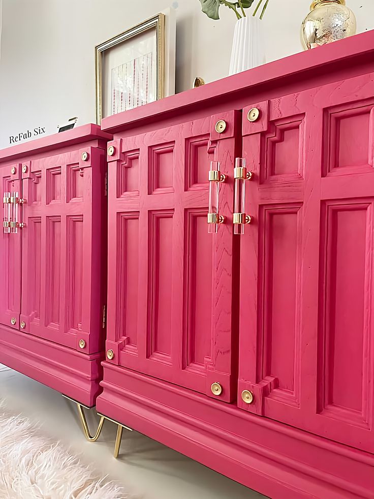 a pink dresser with gold handles and knobs on it's doors, in a living room