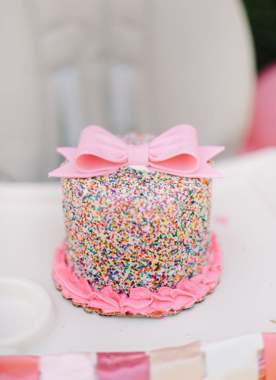 a birthday cake with sprinkles and a pink bow on top is sitting on a table