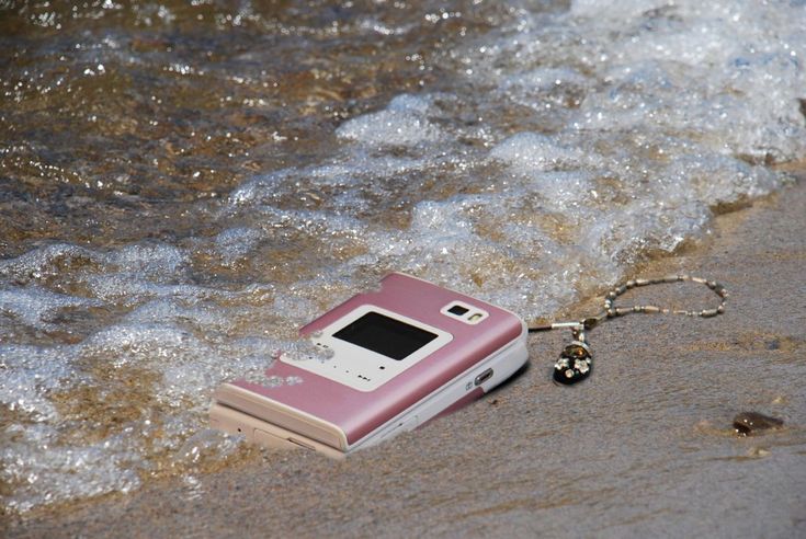 an old cell phone is laying on the sand by the water's edge with a keychain attached to it