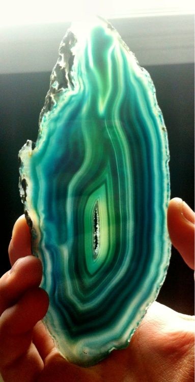 a person holding up a piece of green and blue agate