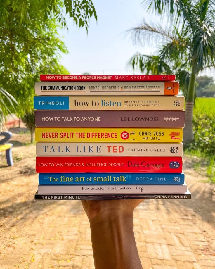 a hand holding a stack of books in front of a dirt road and palm trees