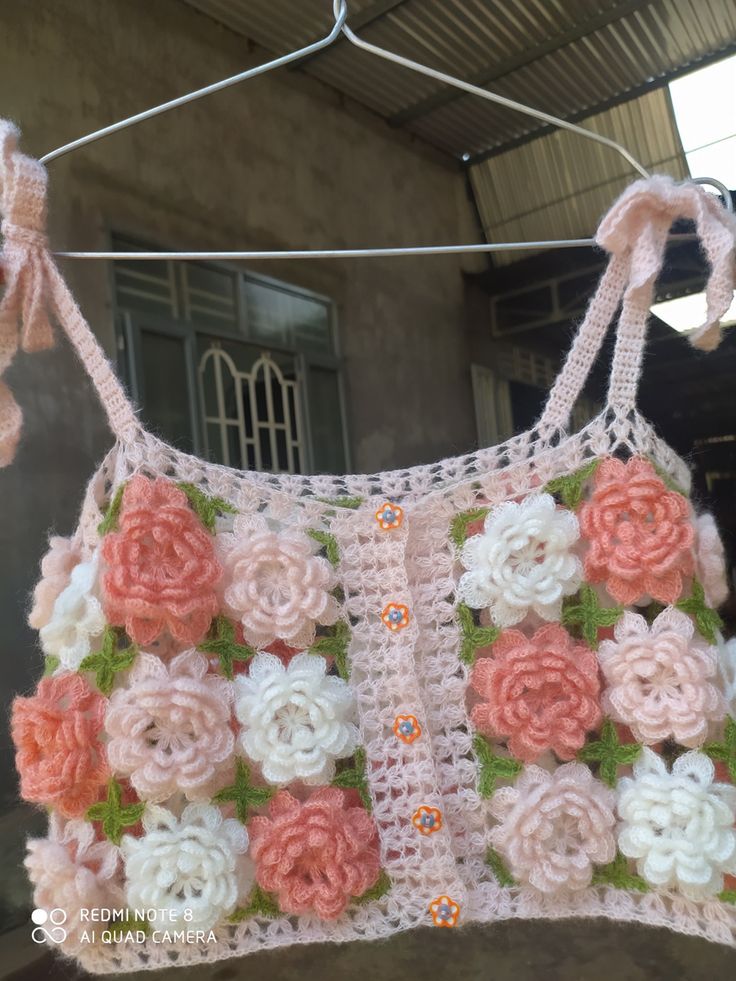 a crocheted pink and white top hanging on a clothes line with flowers in it