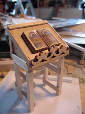 a small wooden table with an open book on it's top, sitting on a workbench