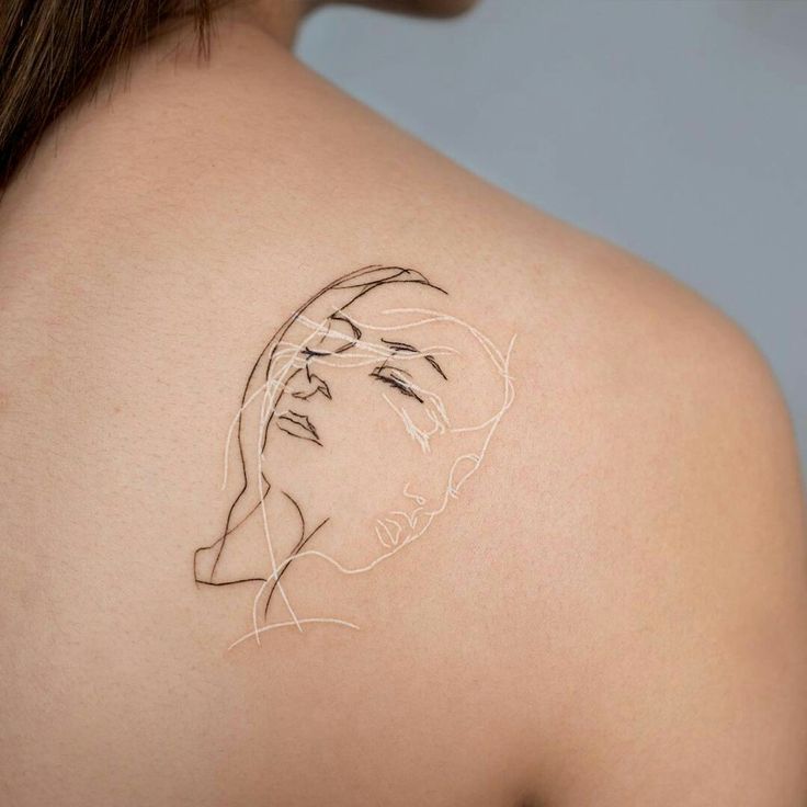 a woman's shoulder with a tattoo on her left arm and the outline of a face