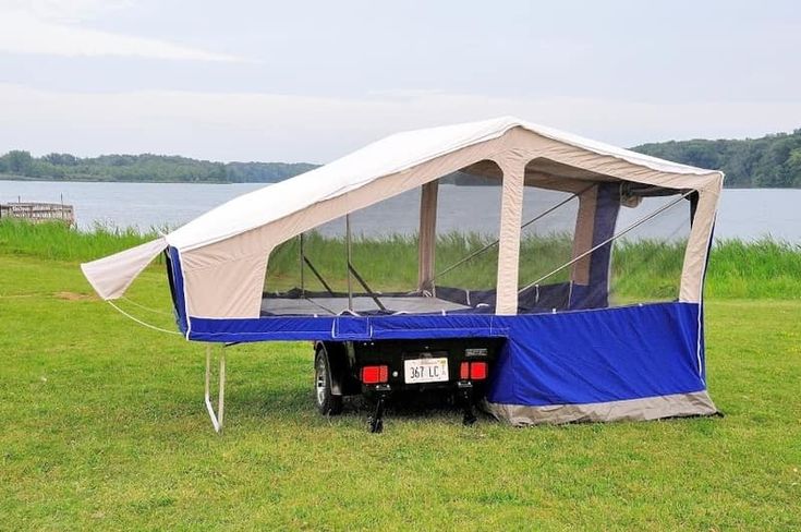 a truck with a tent attached to it parked in the grass near water and trees