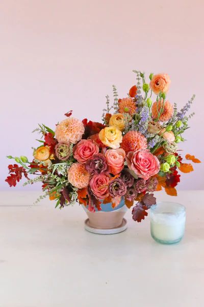 a vase filled with lots of colorful flowers next to a candle on top of a table