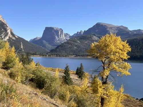 a lake surrounded by mountains and trees with yellow leaves on the grass in front of it