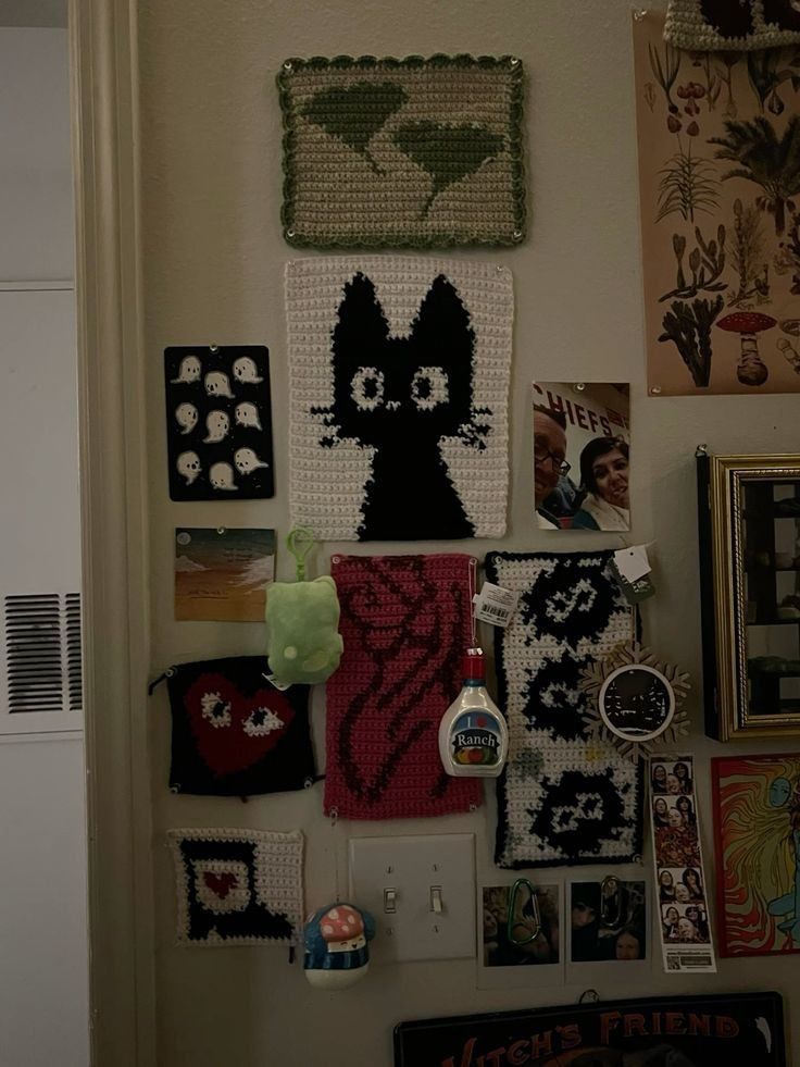 the wall is covered with pictures and crocheted cat art hanging from it's sides