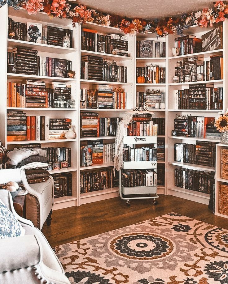 a living room filled with lots of books on top of a white book shelf next to a couch