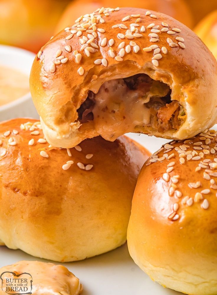 several bagels with sesame seeds and meat in them on a white plate next to oranges