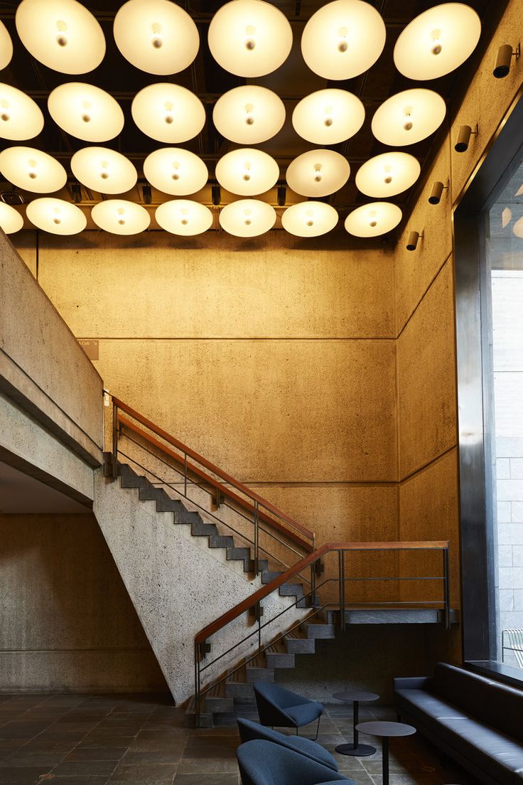 an empty lobby with several chairs and lights on the ceiling, along with a stair case