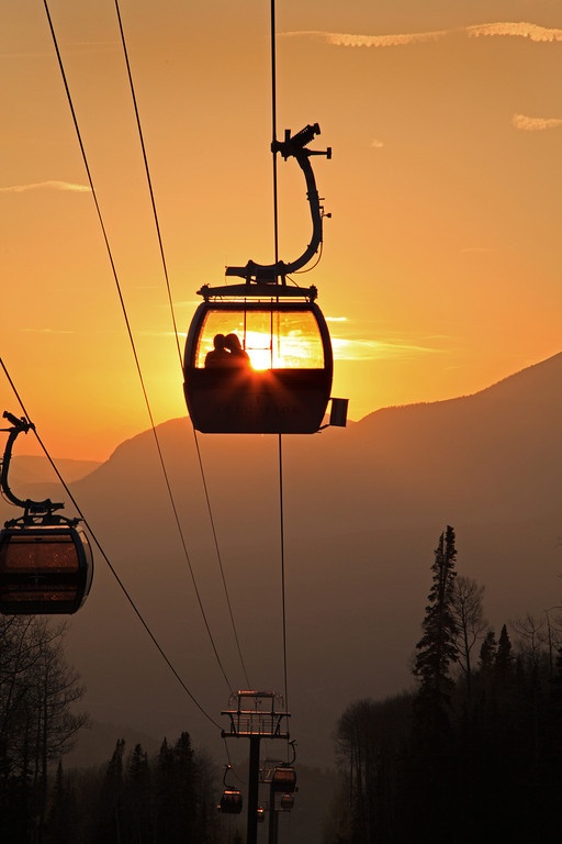 the sun is setting behind a gondola with two people on it and mountains in the background