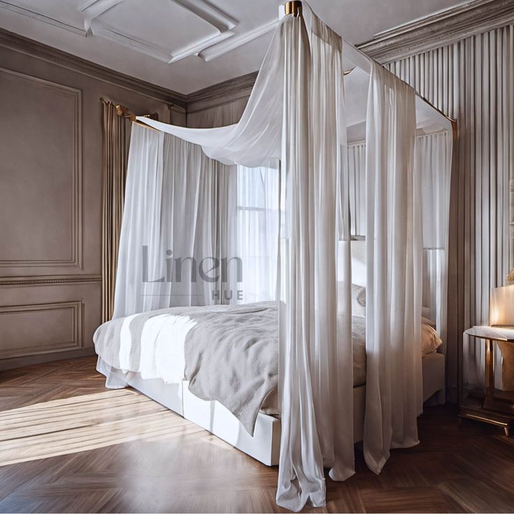 a white canopy bed sitting in a bedroom next to a wooden table and lamp on top of a hard wood floor