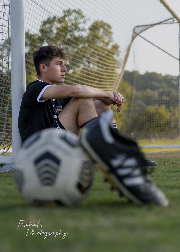 a young man sitting on top of a soccer field next to a goalie's net