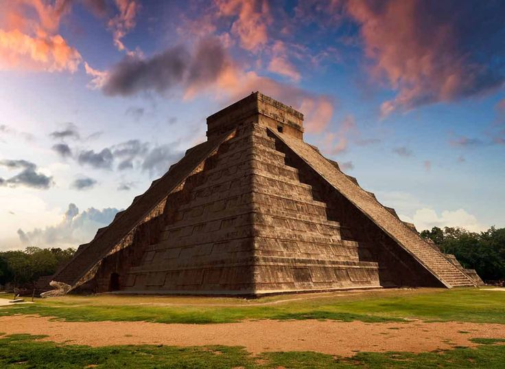 an ancient pyramid in the middle of a grassy area with trees and clouds behind it