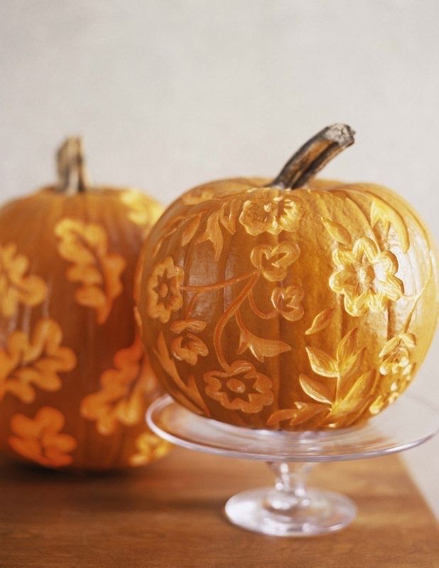 two carved pumpkins sitting on top of a glass stand with flowers and leaves painted on them