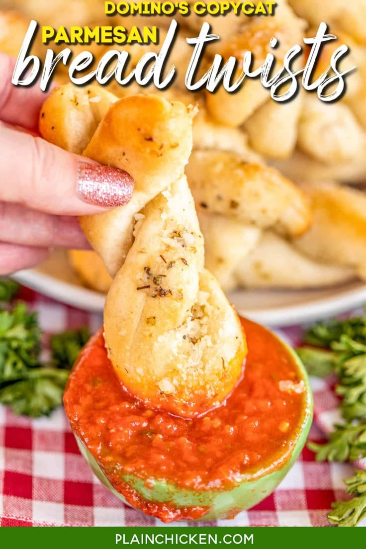 someone dipping bread into a small bowl of tomato sauce with parmesan bread twists in the background