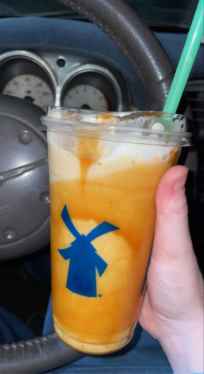 a person holding up a drink with a straw in it's hand and steering wheel behind them