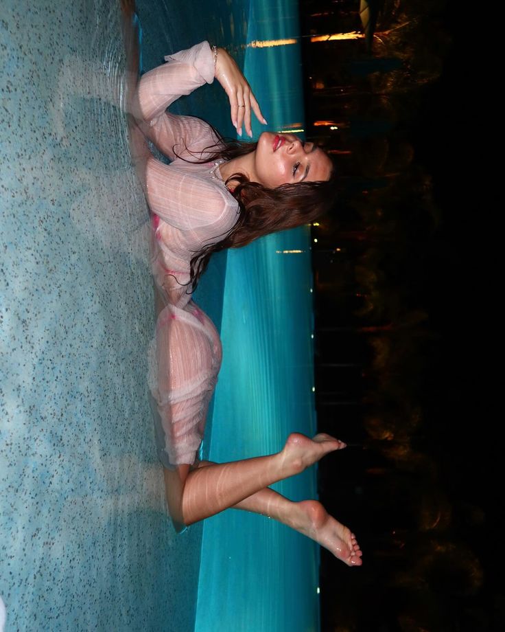 a woman is posing in front of a pool with her feet up on the edge