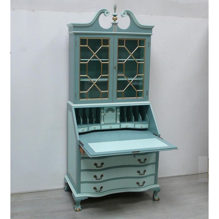 an antique desk with glass doors and drawers on it's top, in front of a white wall