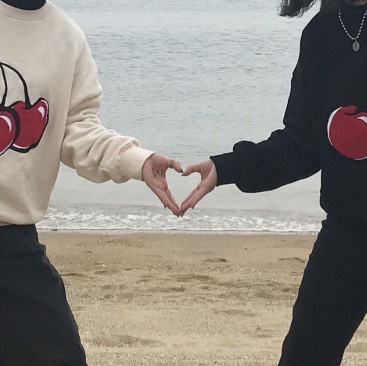 two people holding hands making a heart shape with their hands on the beach near the ocean