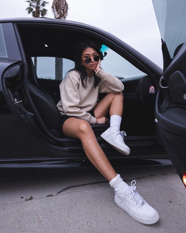 a woman sitting in the door of a car with her legs crossed and wearing white sneakers