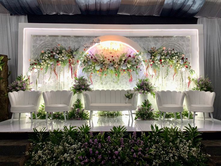 a stage set up with white chairs and flowers