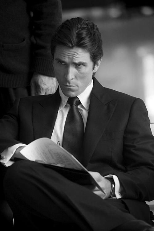 a man in a suit and tie sitting down reading a paper while holding a pen