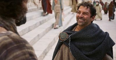 a man smiles as he talks to another man on the steps in front of him