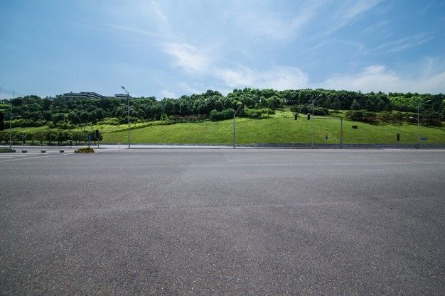 an empty parking lot in front of a grassy hill