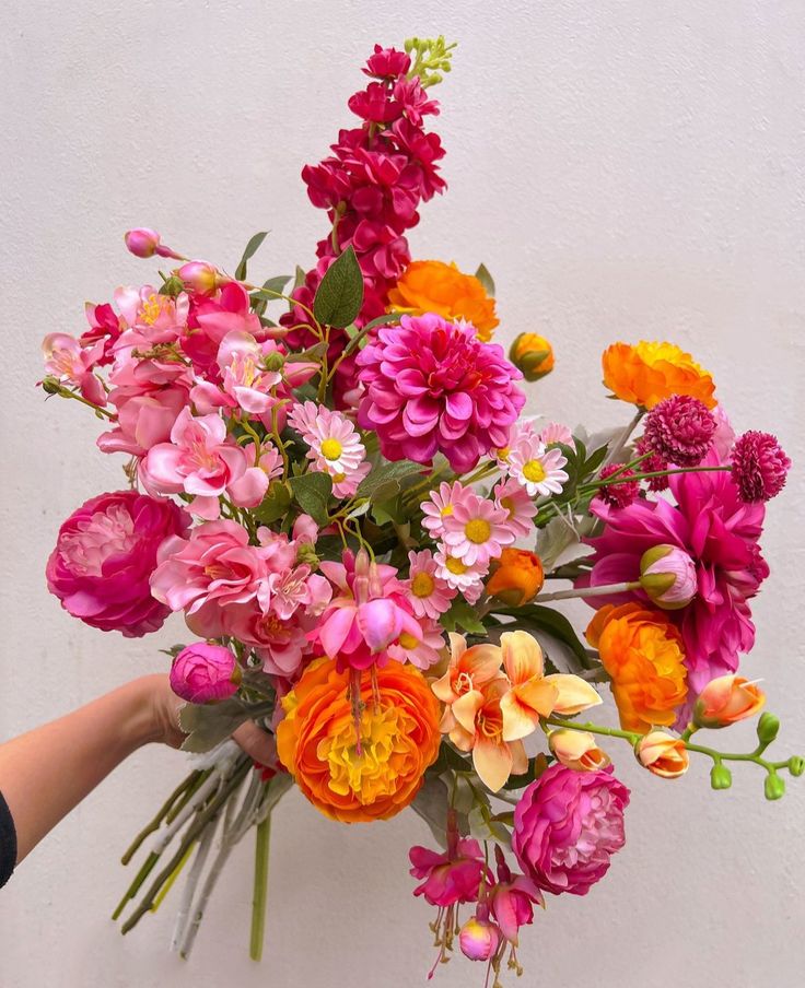 a person holding a bouquet of flowers in their hand on a white wall with pink, orange and yellow colors