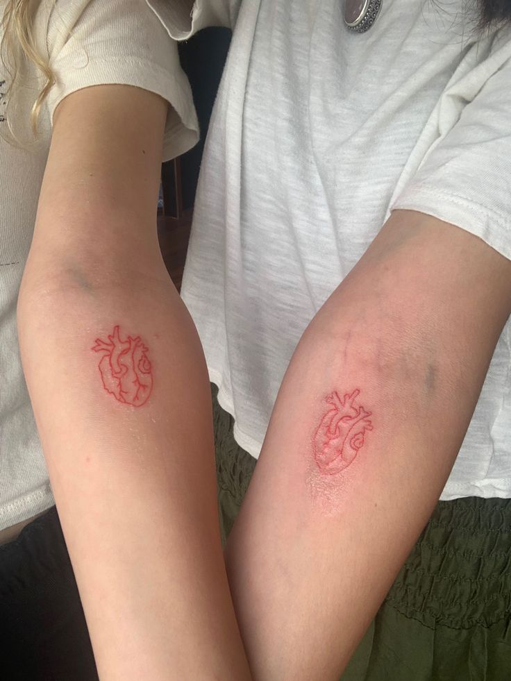 two people with tattoos on their arms and one has a red heart in the middle