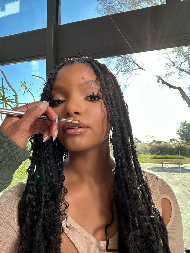 a woman with long dreadlocks is getting her make - up done in front of a window