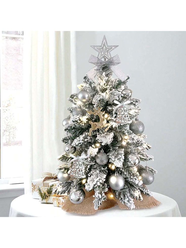 a small christmas tree with silver and gold ornaments on it's base, in front of a window