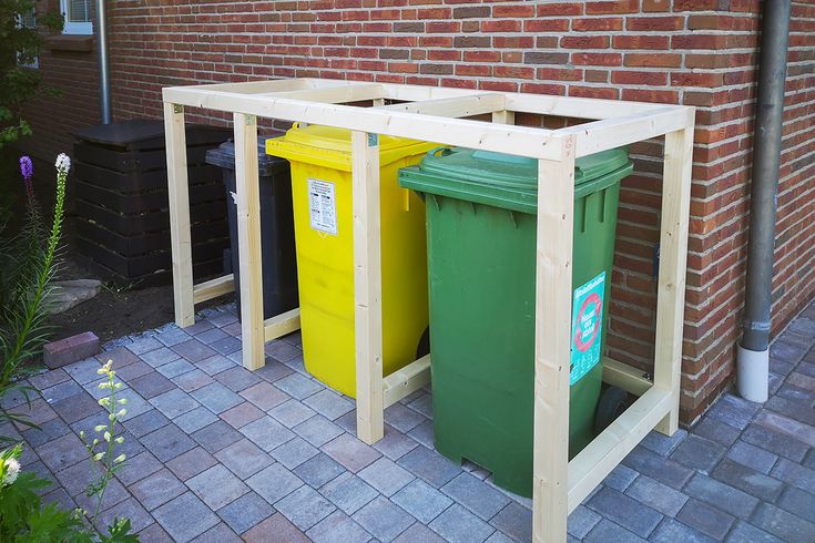 two trash cans sitting next to each other in front of a red brick wall and green bins