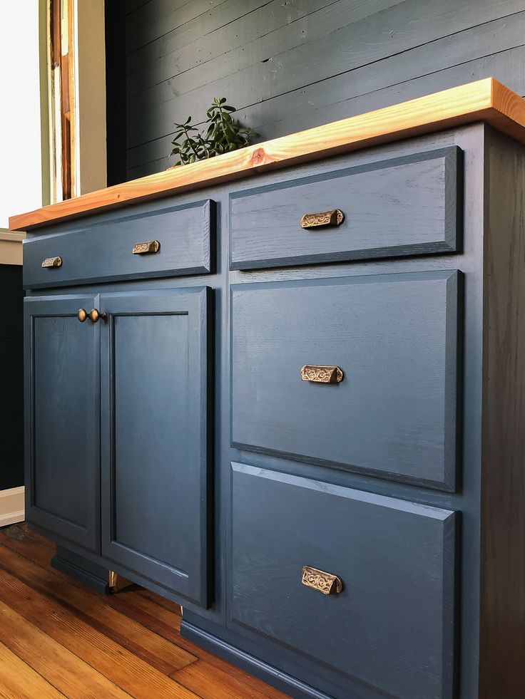 a blue dresser with brass handles and drawers in a room that is painted dark blue