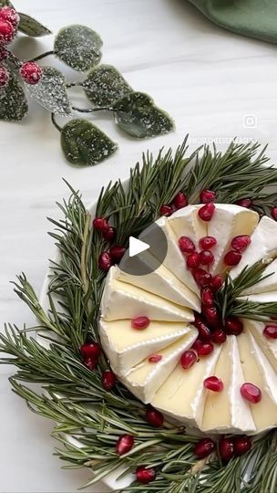 a piece of cheese with pomegranates is on a platter surrounded by greenery