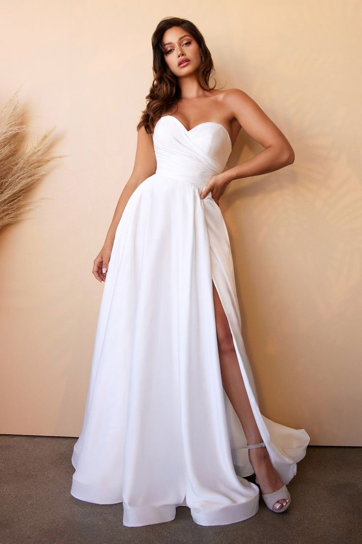 a woman standing in front of a wall wearing a white dress with high slits