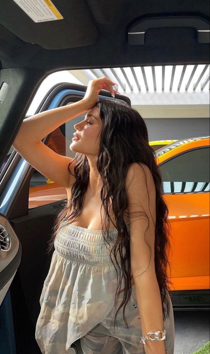 a woman standing in front of a car with her hand on her head and looking out the window