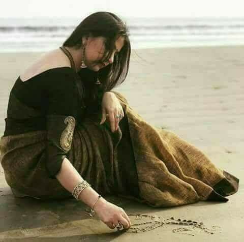 a woman sitting on top of a sandy beach next to the ocean and writing in the sand