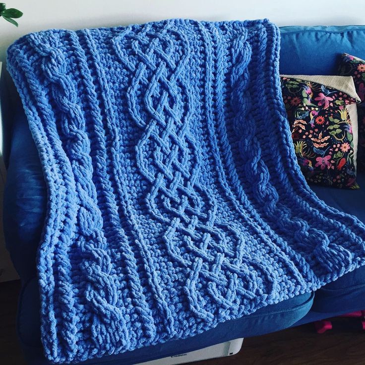 a blue crocheted blanket sitting on top of a blue couch next to pillows