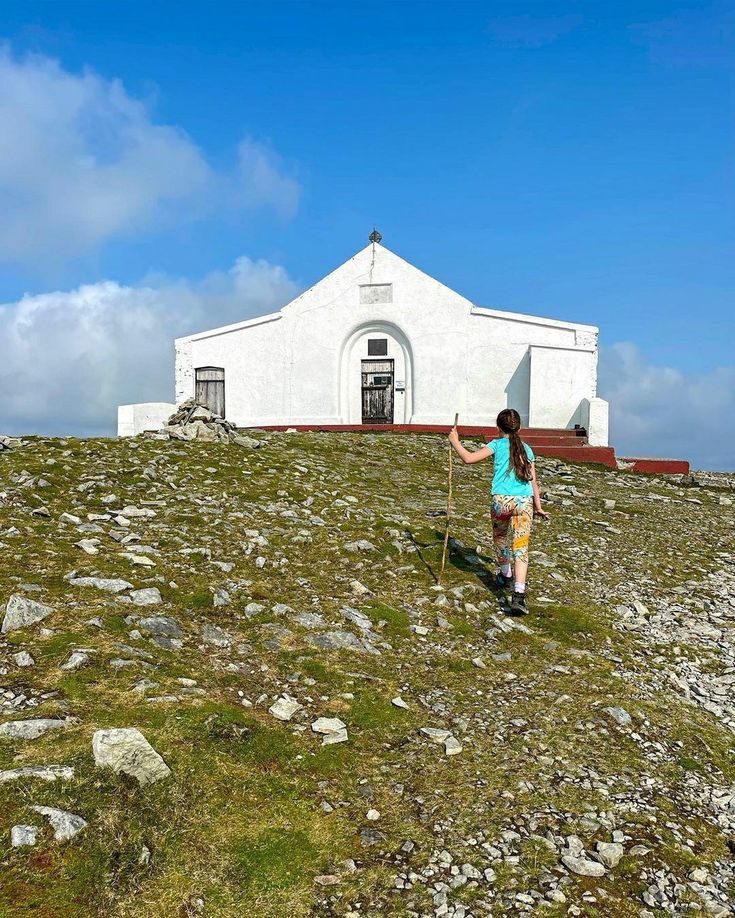 a woman standing on top of a grass covered hill next to a white church building