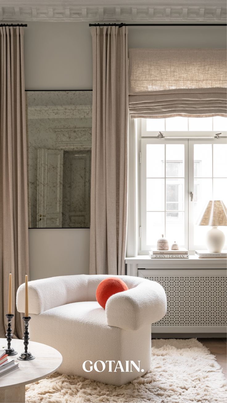 a white chair sitting in front of a window next to a table with candles on it