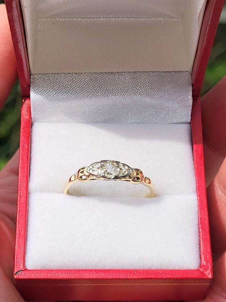 someone is holding an old diamond ring in their red velvet box, which has been opened for display