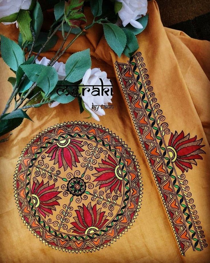 an orange cloth with designs on it and flowers in the middle, sitting next to some green leaves