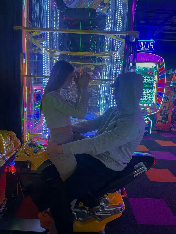 two people are playing video games in a brightly lit room with arcade machines and neon lights